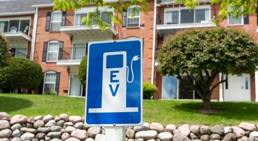 A woman enjoyed her coffee and checks her phone while her EV charges up outside an apartment building